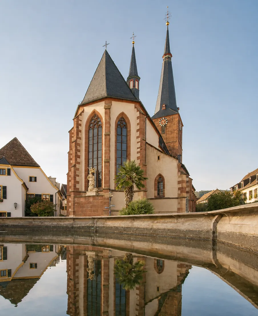 Katholische Pfarrkirche St. Ulrich in Deidesheim mit Spiegelung im historischen Brunnen.