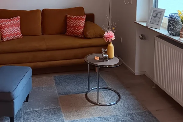 Gemütlicher Wohnbereich der Ferienwohnung Parkblick in Deidesheim mit komfortablem Sofa, Sitzecke und Blick ins Grüne – ideal zum Entspannen nach einem Ausflug an der Deutschen Weinstraße.